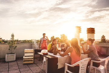 Young friends having barbecue party at sunset on penthouse patio - Happy people doing bbq dinner...