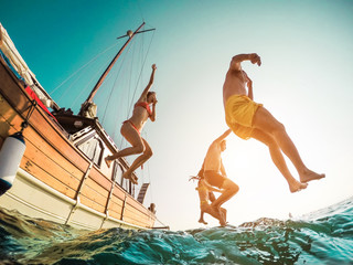 Happy friends diving from sailing boat into the sea - Young people jumping inside ocean in summer...