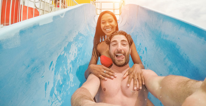 Crazy couple taking selfie photo with action cam in aqua park - Young people having fun in summer holidays with technology trends - Vacation, youth, love and travel concept - Focus on faces