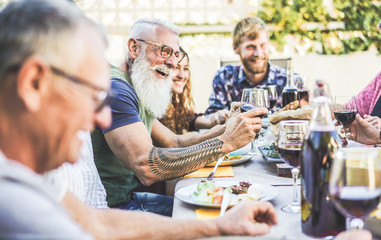Happy family eating and drinking wine at barbecue dinner on patio outdoor - Mature and young people having fun at bbq sunday meal - Food and summer lifestyle concept - Focus on hipster man arm hand