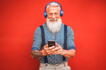 Trendy senior man using smartphone app with red backgorund - Mature fashion male having fun with new trends technology - Tech and joyful elderly lifestyle concept - Focus on his face