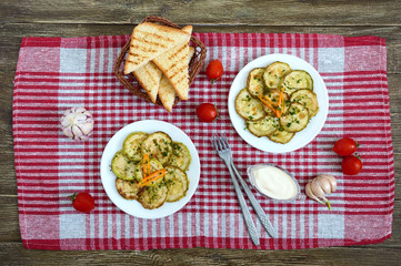 Tasty fried zucchini slices on a plate with sauce on a wooden table. Picnic snack. Rustic style. Top view, flat lay.