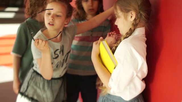 Physical abuse among teens in school. A group of students insult a lonely girl, tear off her glasses. Girl runs away