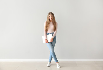 Obraz premium Beautiful young woman with laptop against light wall