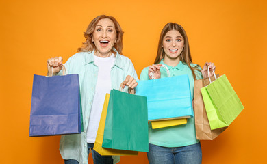 Portrait of happy mother and her daughter with shopping bags on color background