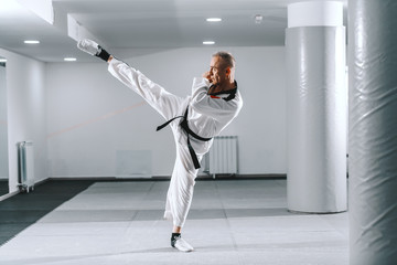 Caucasian trainer in dobok kicking with one leg in gym. Taekwondo class concept.