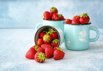 Mugs with ripe red strawberry on color table