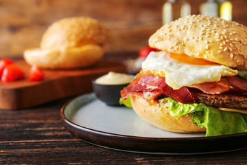 Tasty burger with bacon and fried egg on table