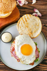 Tasty burger with bacon and fried egg on table