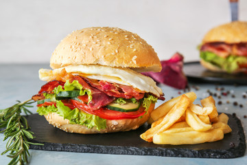 Tasty burger with bacon and french fries on table