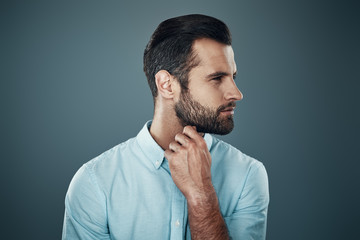 Thinking about... Handsome young man smiling and looking away while standing against grey background