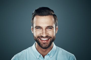 Sincere smile. Handsome young man smiling and looking at camera while standing against grey background