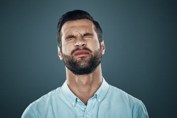 No! Frustrated young man keeping eyes closed while standing against grey background