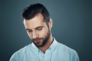 Lost in thoughts. Handsome young man looking down while standing against grey background