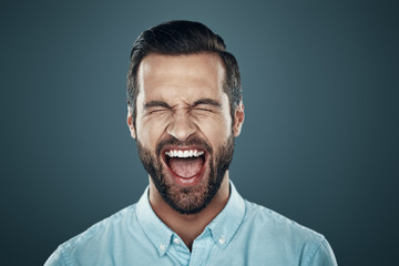 So much fun!. Handsome young man laughing while standing against grey background