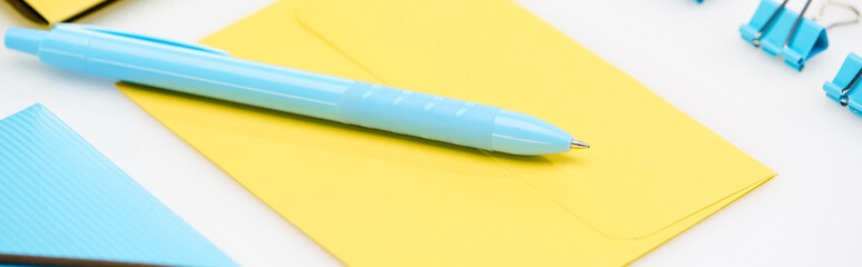 panoramic shot of blue folder, paper clips and pen on yellow envelope on white background