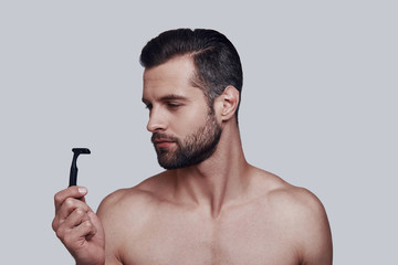 Everything must be perfect. Handsome young man shaving while standing against grey background