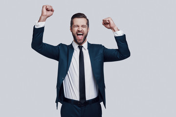 Success! Handsome young man cheering and smiling while standing against grey background