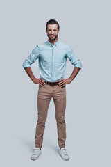 Confidence and charisma. Full length of handsome young man looking at camera and smiling while standing against grey background