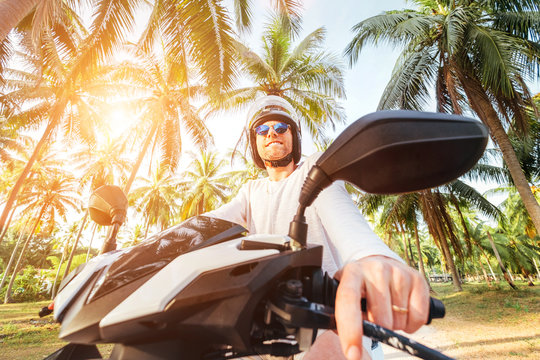 Cheerful man in safe helmet riding a motorbike under palm trees wide angle lens shot