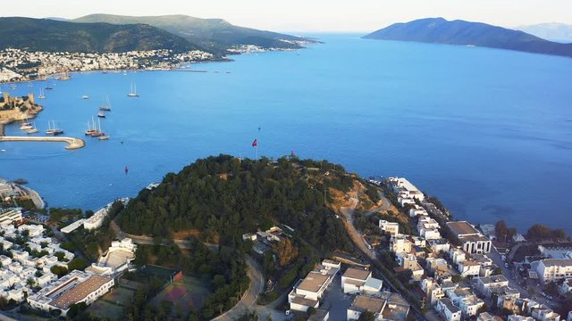 Aerial shot orbiting around hill with red turkish flag on top of it in resort town Bodrum, Turkey. Welcome to Turkey concept 4k