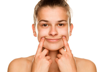 Young woman forcing her smile with her fingers on white background