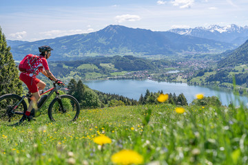 senior woman riding her electric mountain bike in springtimeon the mountains above the Alpsee near Immenstadt, Allgau,Bavaria, Germany