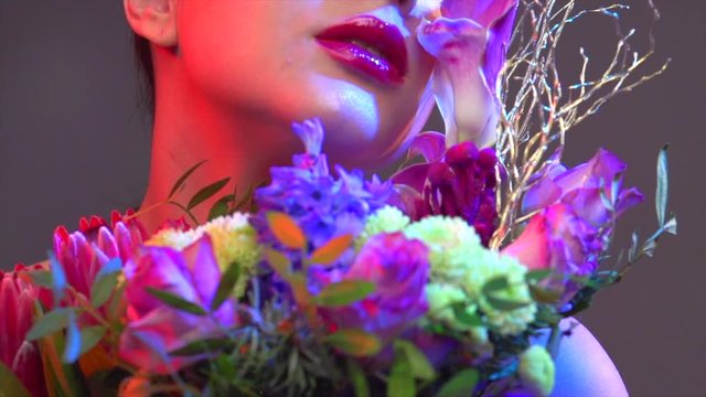 Sexy brunette model girl with bouquet of beautiful flowers. Beauty young woman with bunch of flowers in colorful neon lights. Art design. Slow motion 4K UHD video footage. 3840X2160