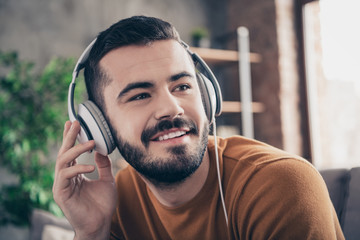 Close up photo of lovely handsome trendy stylish man hold hand use modern technology hear favorite soundtrack sound track orange pullover sweater sit divan couch room