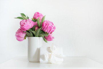 Bouquet of pink peony in vase with gift on white. Copy space for text. Mothers day.