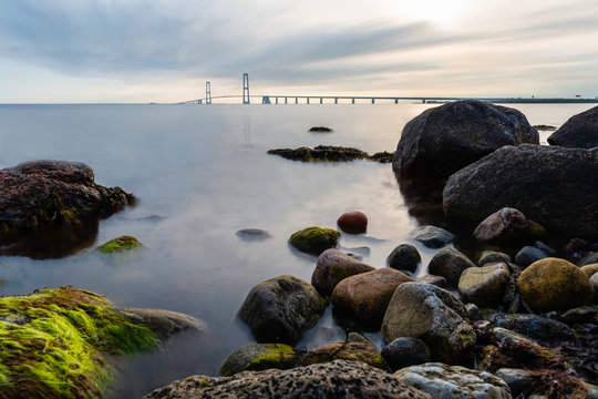 The East Bridge of the Great Belt Bridge from the Granskoven strand in Denmark with colorful rocks and the sea in the foreground