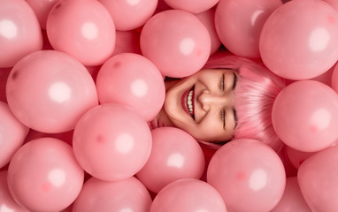 Fototapeta na wymiar Cheerful ethnic woman in pink wig lying under balloons