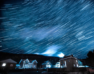Winter landscape with star trails above houses and forest at starry night