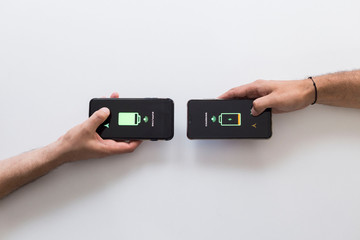 Two hands holding black smart phones while they are wireless charging.