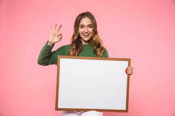 Happy blonde woman holding blank board and showing ok sign