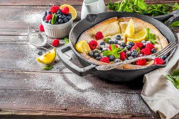 Sweet breakfast vegan dutch baby baked pancake with fruit and berries, wooden background copy space