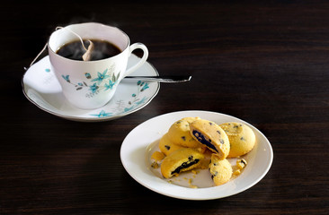 Chocolate chip cookies in white dish and hot tea bag in cup on dark brown background