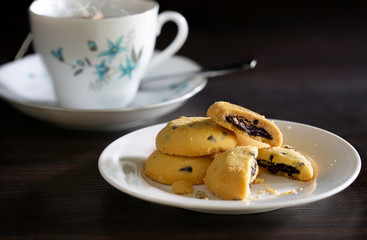 Chocolate chip cookies in white dish and hot tea bag in cup on dark brown background , still life image
