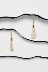 Shot of long beige tassel earrings with triangle-shaped pins. The accessory set is isolated asymmetrically on white background between black faux leather stripes. Fashionable women's fashion item.
