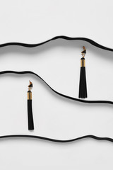 Shot of long black tassel earrings with triangle-shaped pins. The accessory set is isolated asymmetrically on white background between black faux leather stripes. Fashionable women's fashion item.