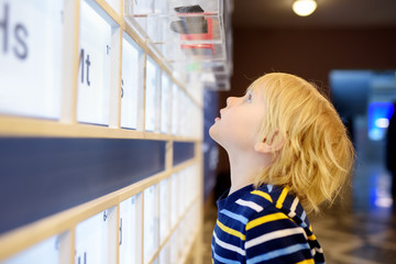 Little сaucasian boy is looking an exposition in a scientific museum. Periodic table of chemical...