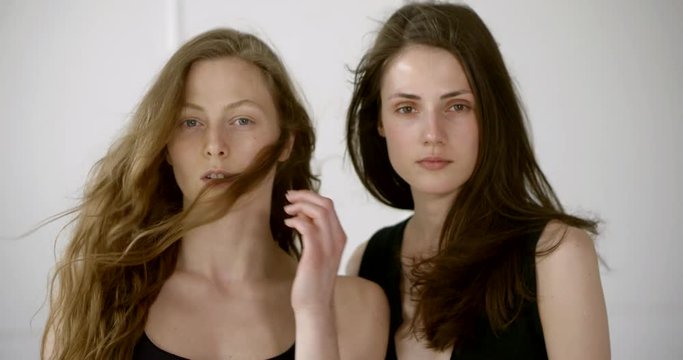 two charming models girls are posing in studio, close-up of faces, fan is blowing