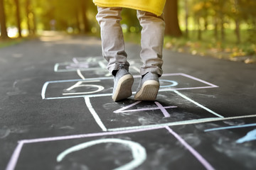 Closeup of little boy's legs and hopscotch drawn on asphalt. Child playing hopscotch game on...