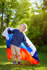 Portrait of cute little boy in public summer park with russian flag on background. Fans child supporting and cheering their national team. Day of independence.