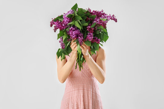 Beautiful young woman with bouquet of lilac flowers on white background