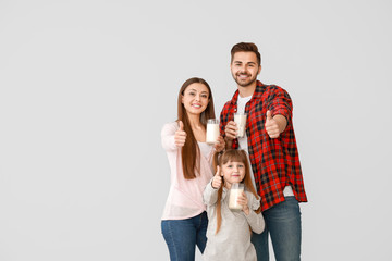 Young family with glasses of tasty milk showing thumb-up gesture on light background