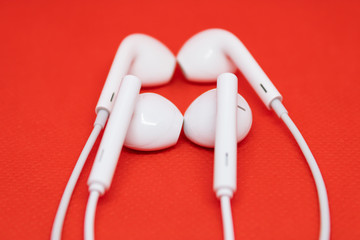 Two pairs of white headphones close to each other on red background, one pair of earphones is blurred - Image