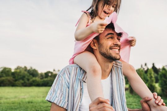 Handsome dad is spending time with his little charming daughter outdoors. Image of happy cute little girl playing with father in the park during the sunset. Fathers Day. Daddy and daughter shares love