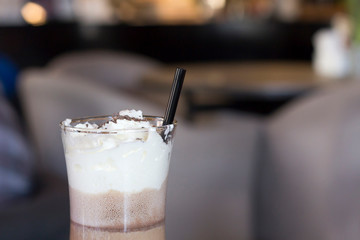 Hot coffee drink with whipped cream in glass, black straw in cafe. Close-up, copy space, toned