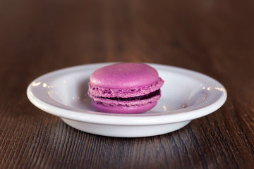 Pink macaroon in white plate on dark wooden table, toned. Close-up, copy space